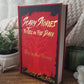 Book titled 'Scary Stories to Tell in the Dark' on a wooden surface with a plant and textured fabric in the background.